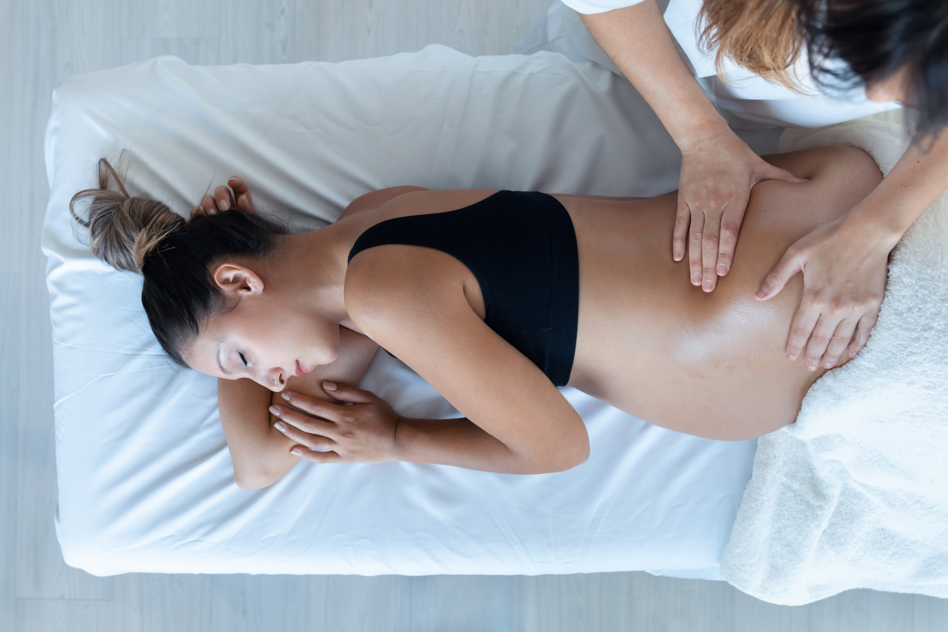 Shot of beautiful young physiotherapist woman massaging tummy on pretty pregnant woman on a stretcher at home.